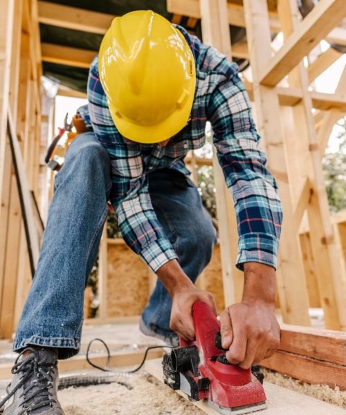 construction-worker-with-hard-hat-sanding-down-wood-piece construction-worker-with-hard-hat-sanding-down-wood-piece